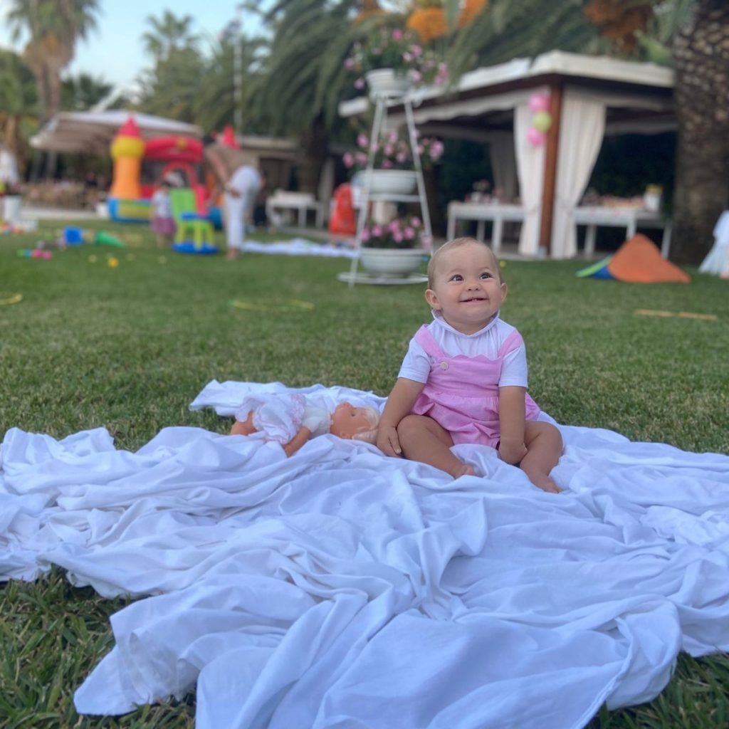 Bimba seduta su un telo bianco sul prato durante una festa in giardino